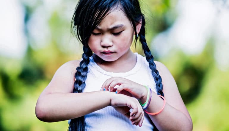 upset child with long braids and colorful accessories scratches wrist