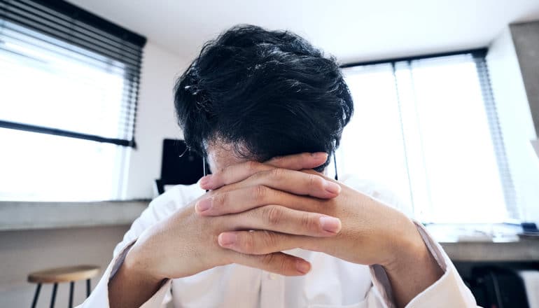 A man looks down and covers his face while on a video conference call