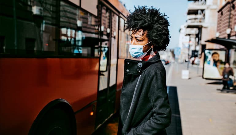 A woman stands on the sidewalk next to a city bus