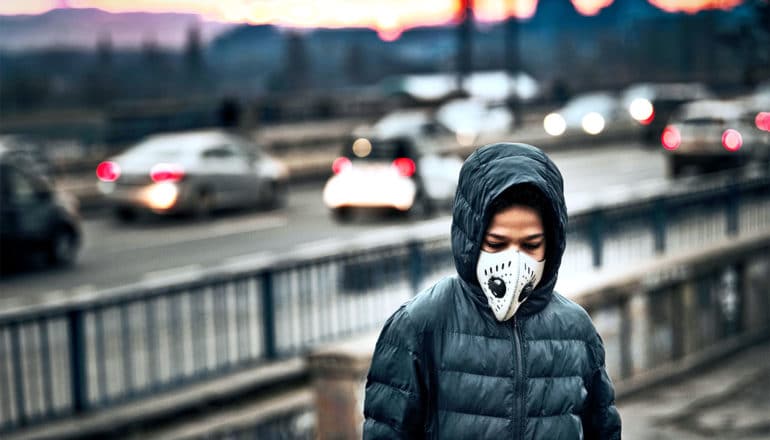 A young boy walks by the side of a road wearing a face mask