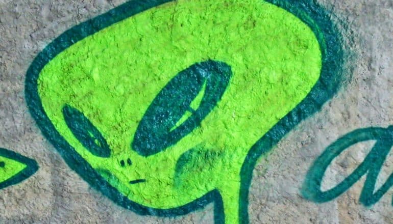 A green alien painted on a concrete wall