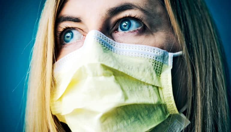 A woman wearing a yellow face mask looks into the distance with worry