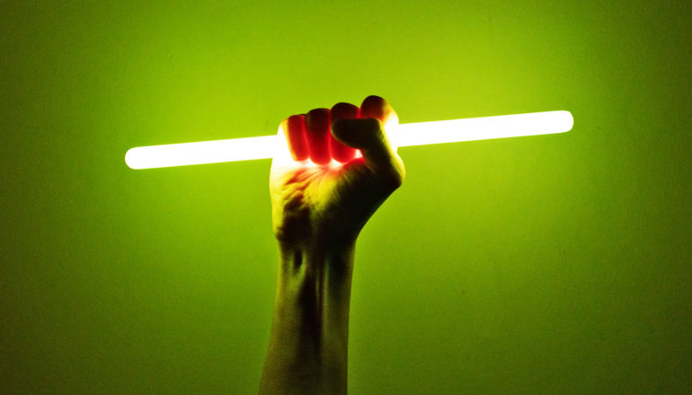 A hand holds a glowing stick of light against a green background