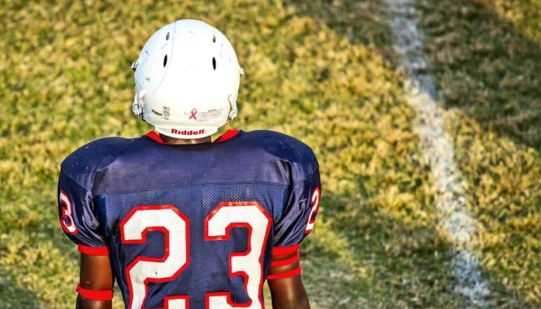 A young football player looks towards the field while wearing a jersey with number 23