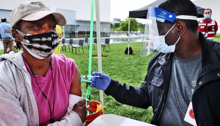 A woman gets a COVID-19 vaccine from a health worker while outside under a tent