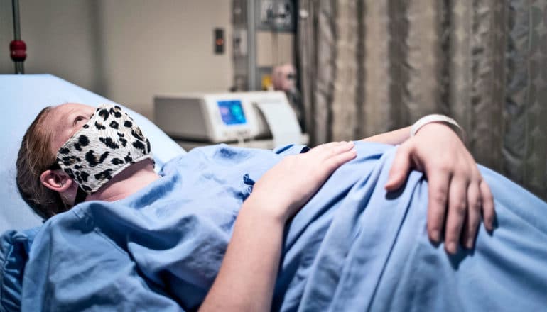 A pregnant woman in a hospital bed wearing a face mask