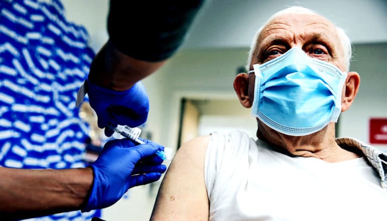 An older man gets a COVID-19 vaccine while wearing a face mask