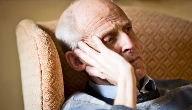 An older man in a chair touches the side of his head