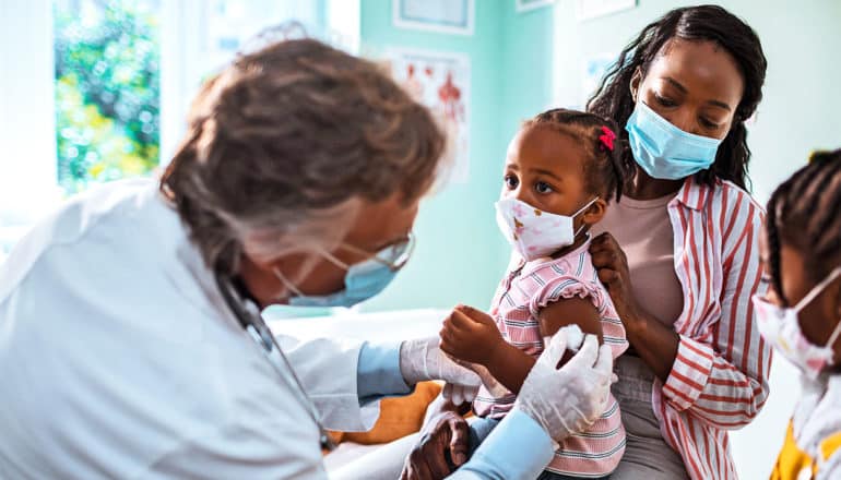 A mother holds her little girl as the doctor gives her a shot