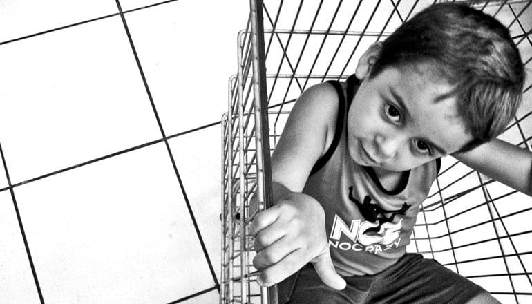 A child in a grocery cart looks up at the cart