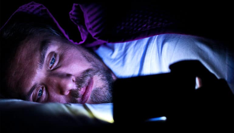 A man lays awake in bed looking at his phone