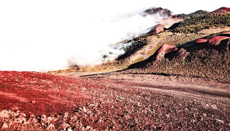 A landscape of red dirt with ash or fog rolling over the horizon