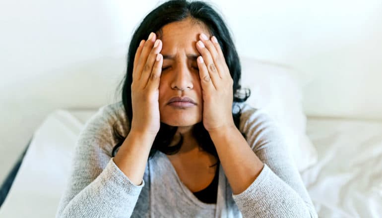 A woman holds her head in her hands while sitting up in bed