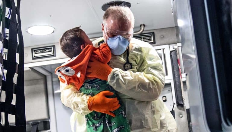 An EMT carries a very young child from the back of an ambulance