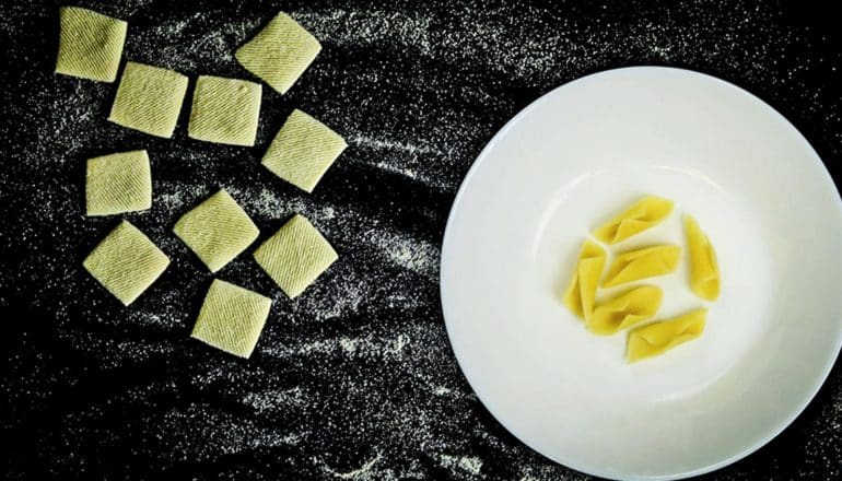 The uncooked pasta sits flat, while the cooked pasta has curled into a tube-like shape