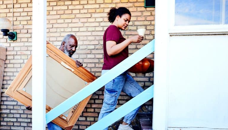 A father and daughter carry items up stairs into a house