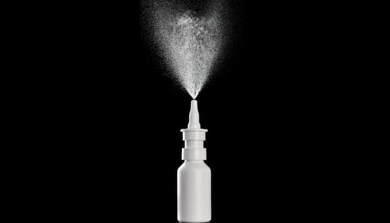 A nasal spray bottle on a black background sprays mist into the air