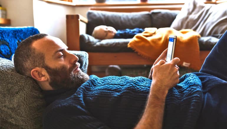 A man laying on the floor reads his phone