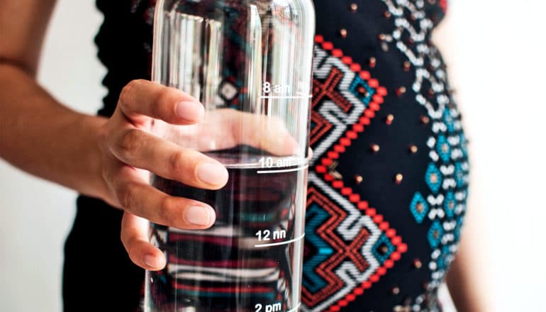 A pregnant woman holds a large reusable water bottle