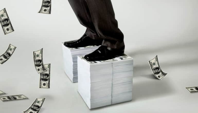 cropped view of dress shoes of someone standing on stack of money