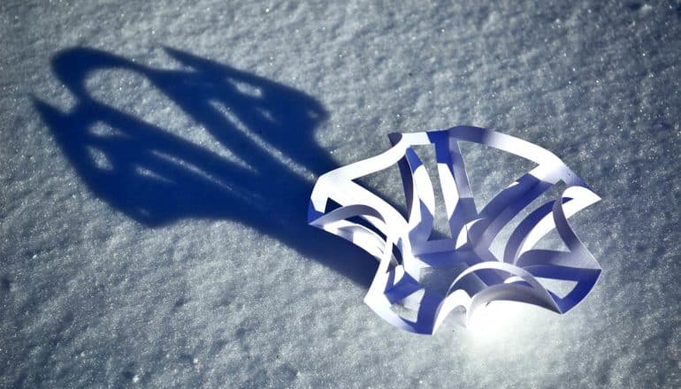 A kirigami design sits on a white surface with a light casting a shadow behind it
