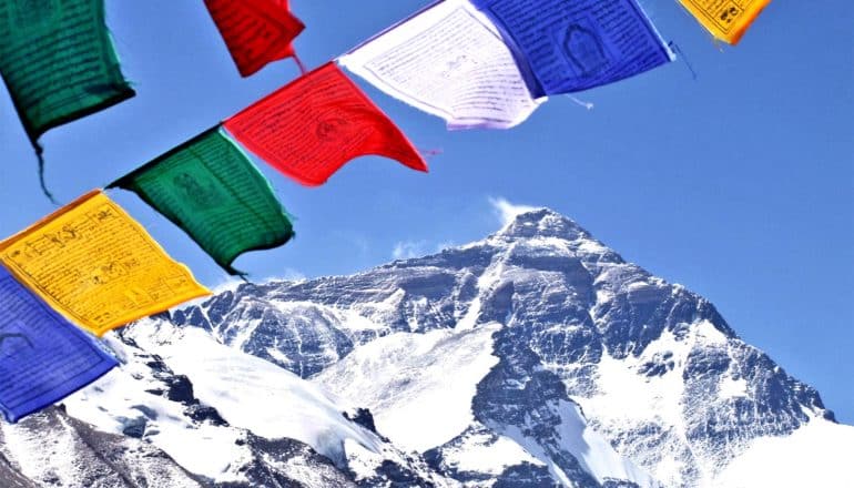 Colorful prayer flags flutter in the wind with the north face of Everest in the background