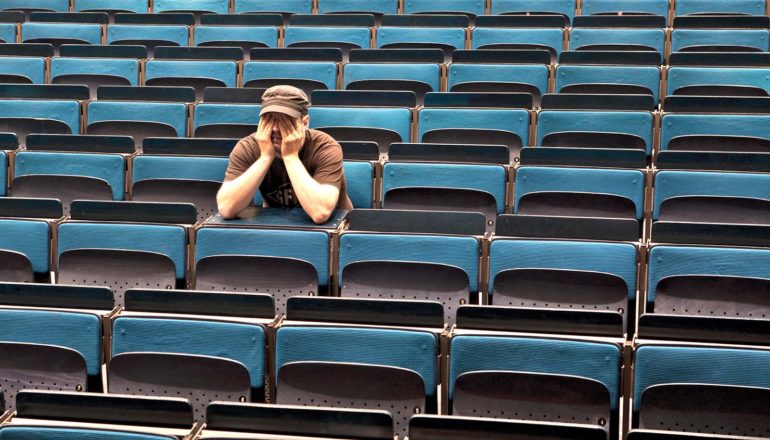 one person in empty auditorium seating with hands over eyes