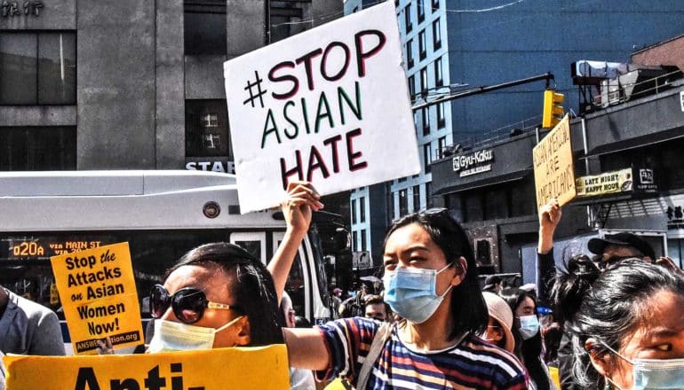 A woman at a protest holds a sign that reads #StopAsianHate