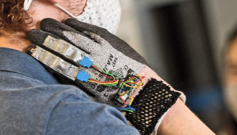 hand in glove with wires reaches for hair below person's ear