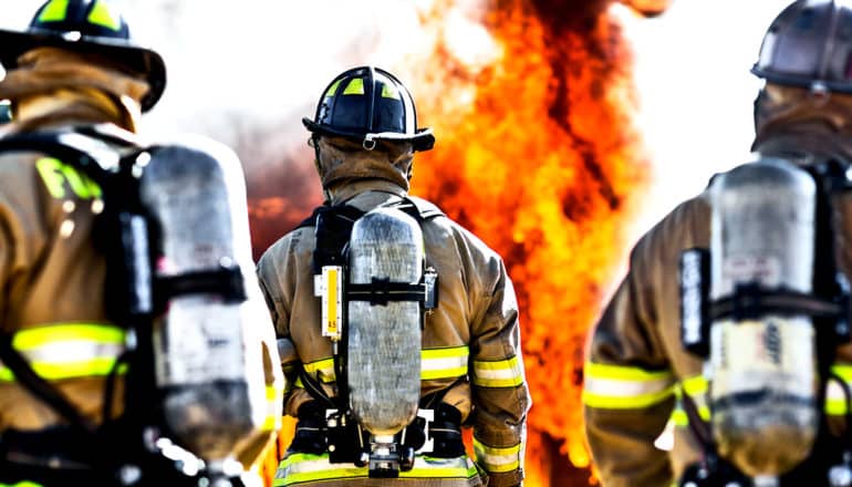 Three firefighters wearing full gear walk towards a fire