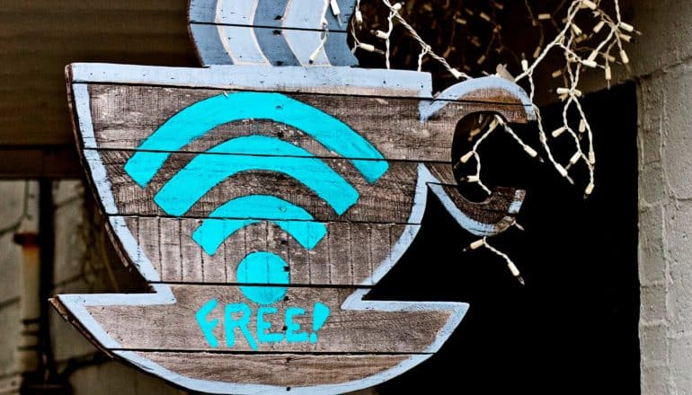 A coffee shop sign in the shape of a coffee mug has a blue WiFi signal symbol above the word "FREE!" on it