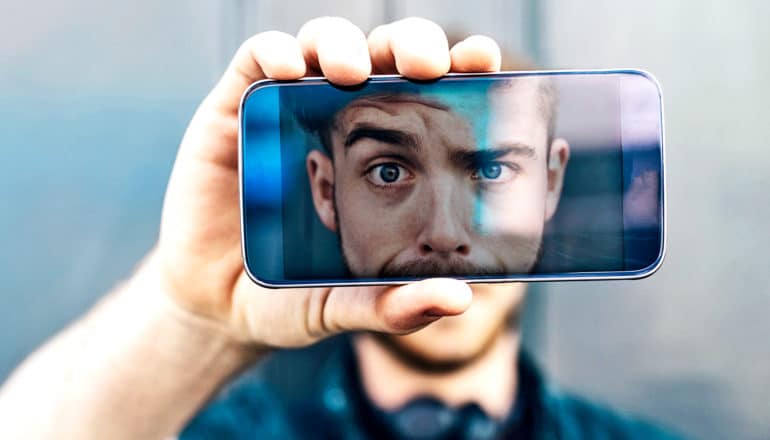 A man holds his phone in front of his face so that it's visible on the screen