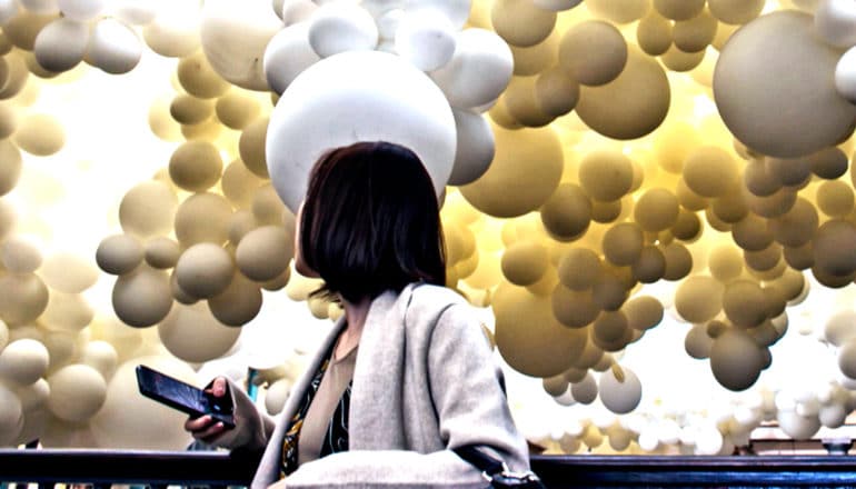 A woman looks over her shoulder to see huge yellow and white balloons filling the sky behind her