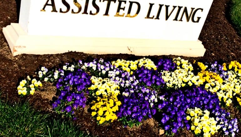 An assisted living facility sign with flowers planted in front of it