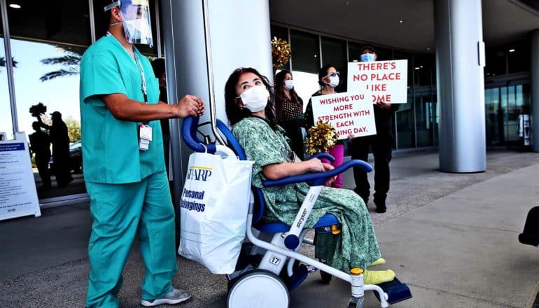 A woman leaves the hospital in a wheelchair while wearing a face mask