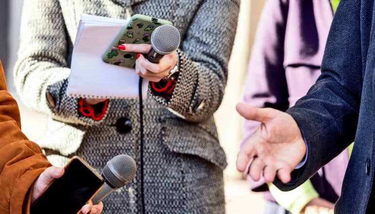 hands hold mics, notebooks, phones