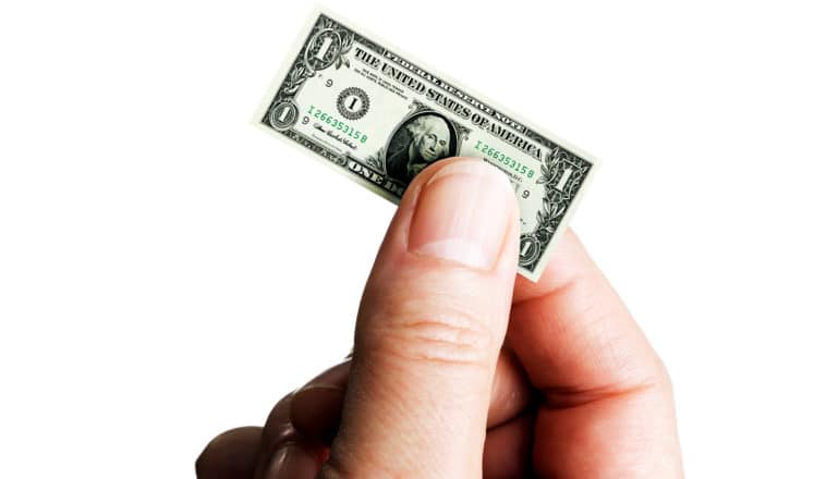 A person holds a tiny dollar bill between their thumb and forefinger