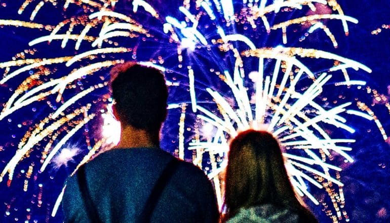 Two people stand looking up watching fireworks