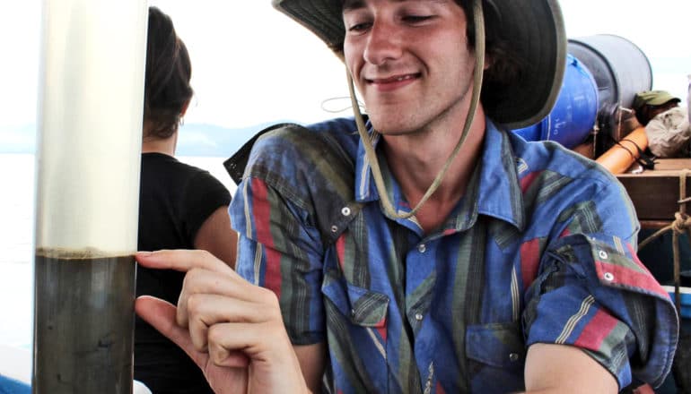 A smiling research places his thumb and forefinger against the sediment core