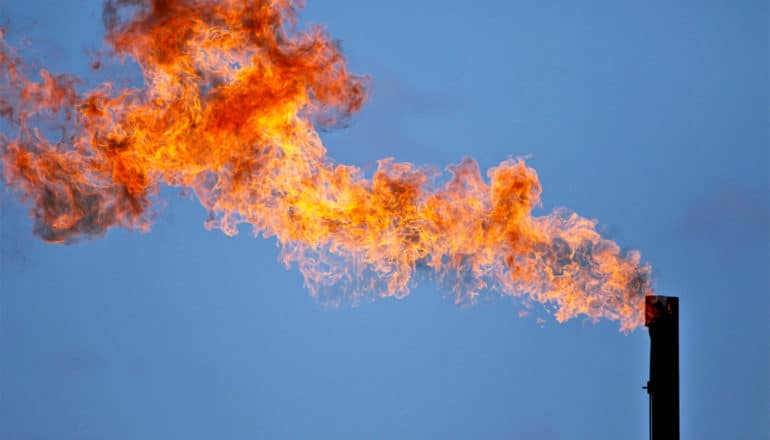 Methane flaring causes a plume of flame from a pipe against a blue sky