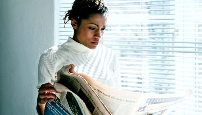 A woman reads a newspaper by a window