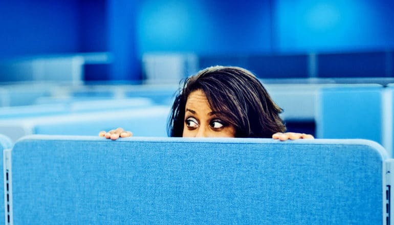 An office worker peeks over a blue cubicle wall