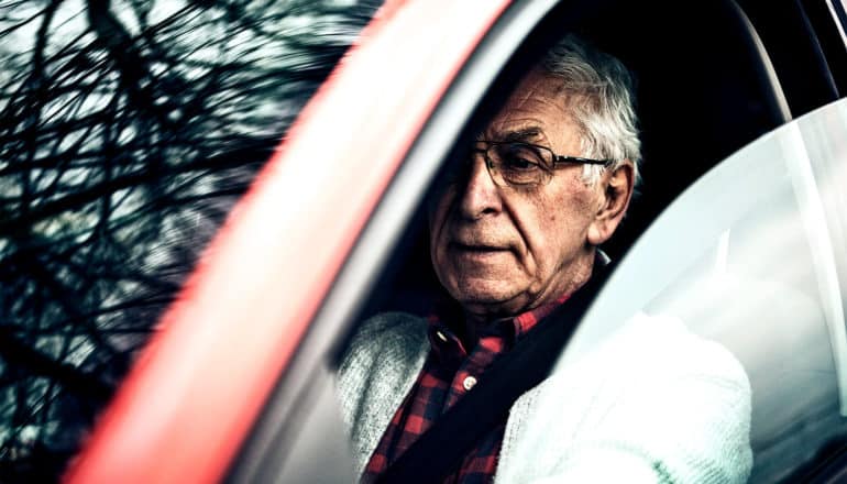 An older adult man sits behind the wheel in a car