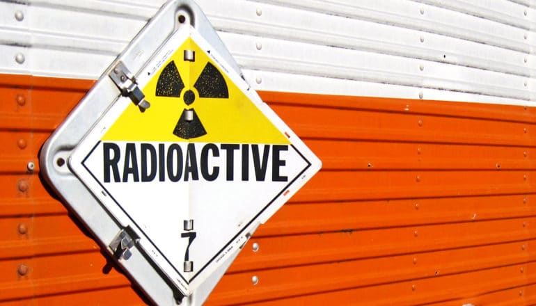 A sign on the side of a white and orange truck trailer reads "Radioactive"