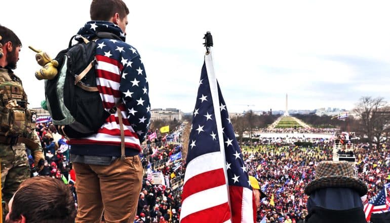 A man wearing an American flag hoodie looks over the January 6th insurrection at the US Capitol