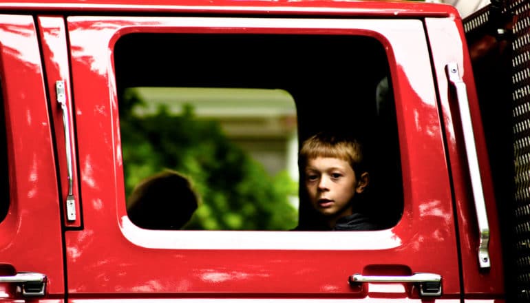 child's face in extended cab window of red truck