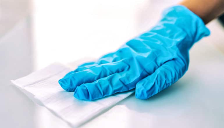 A person wearing a blue glove wipes down a surface