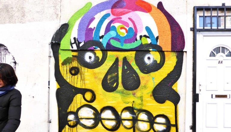 A painting of a skull on the side of a building with colorful swirls where a brain should be