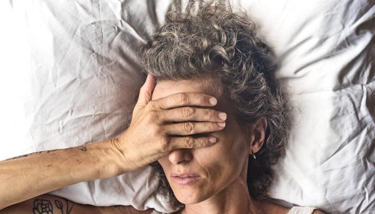 A woman laying on a white pillow puts her hand over her face