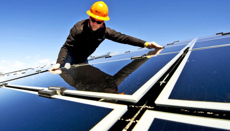 A man wearing a hard had installs a solar panel